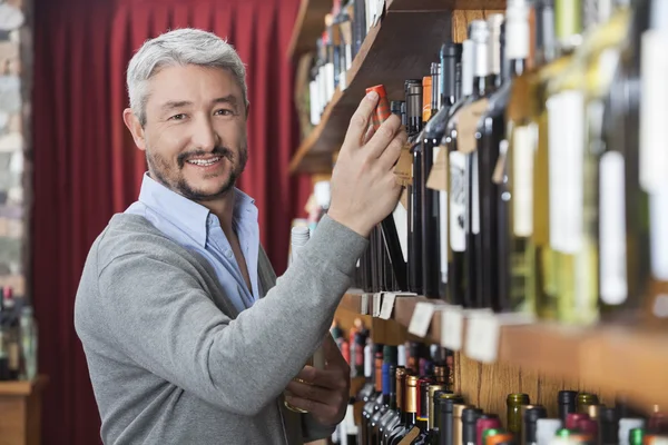 Cliente maduro eligiendo botella de vino en la tienda —  Fotos de Stock