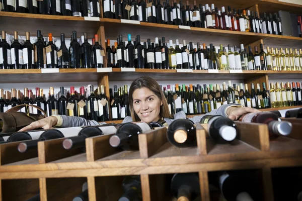 Mulher feliz que se inclina na cremalheira do vinho na loja — Fotografia de Stock