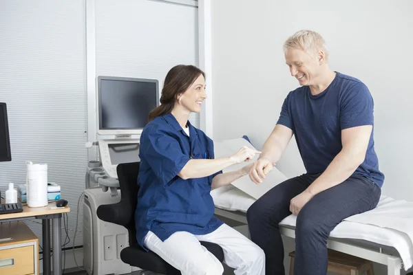 Lachende arts aanraken van de mannelijke patiënten Hand In kliniek — Stockfoto