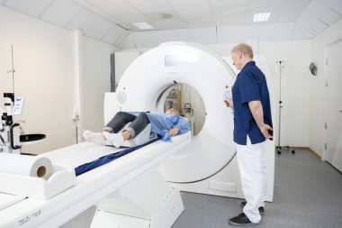Patient Lying On MRI Machine While Male Doctor Operating It clipart
