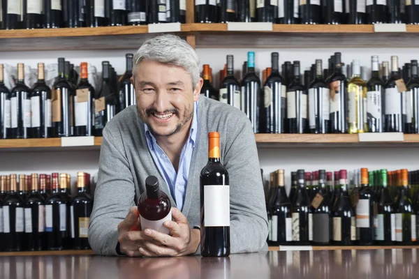 Szczęśliwy człowiek, trzymając butelkę wina podczas oparty na tabeli — Zdjęcie stockowe