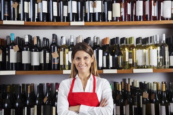 Feliz vendedora de pé contra prateleiras na loja de vinhos — Fotografia de Stock