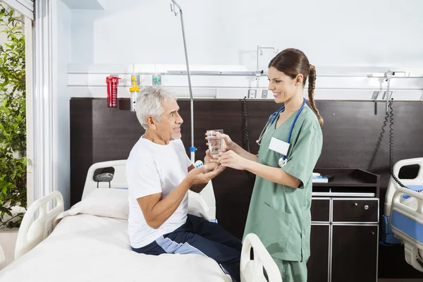 Медсестра дает лекарство и воду старшему пациенту — стоковое фото