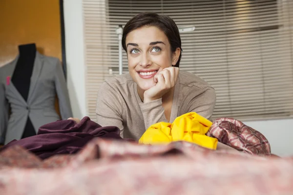 Sastre reflexivo sonriendo mientras se apoya en el banco de trabajo — Foto de Stock