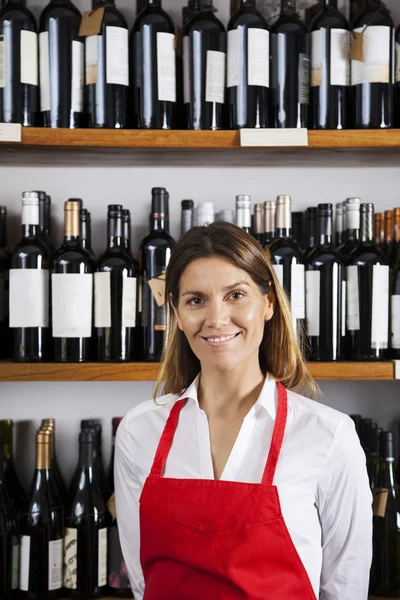Vendedora confiante em pé contra prateleiras na loja de vinhos — Fotografia de Stock