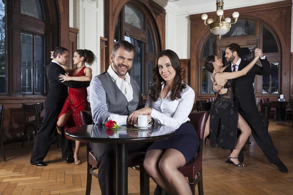 Casal sorridente sentado na mesa enquanto dançarinos realizando tango — Fotografia de Stock