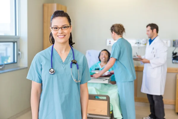 Enfermeira sorrindo com paciente e equipe médica no fundo — Fotografia de Stock