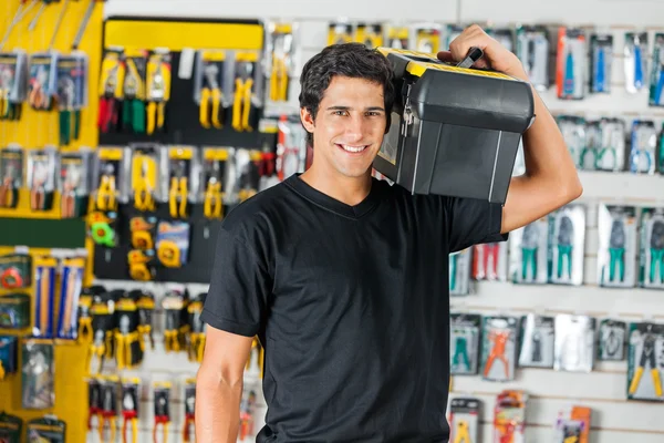 Hombre sonriente llevando la caja de herramientas en el hombro en la tienda — Foto de Stock