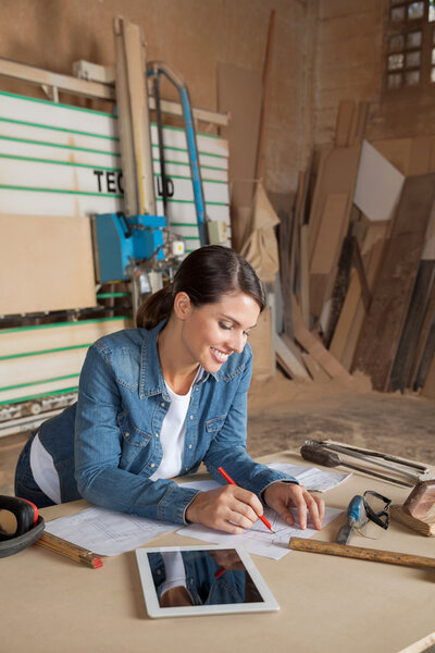 Female Carpenter Working On Blueprint In Workshop