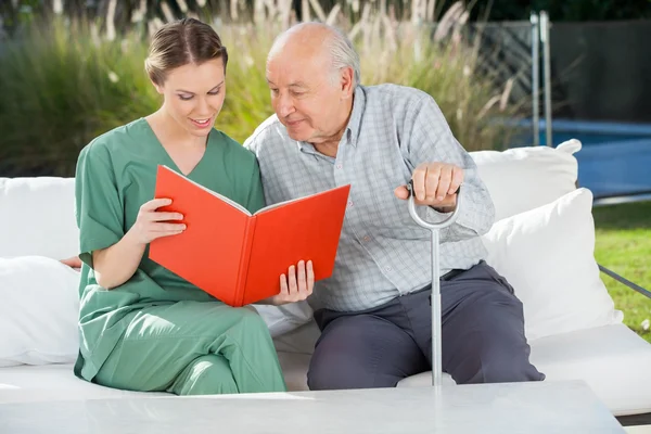 Senior Man lezing boek met vrouwelijke Caretaker op Bank — Stockfoto