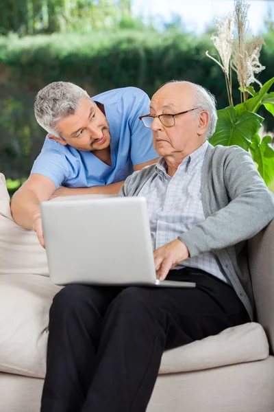 Männliche Krankenschwester unterstützt älteren Mann bei der Verwendung von Laptop — Stockfoto