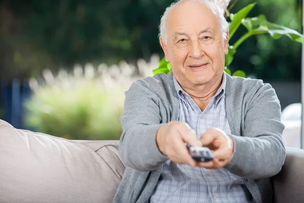 Älterer Mann benutzt Fernbedienung während er auf der Couch sitzt — Stockfoto