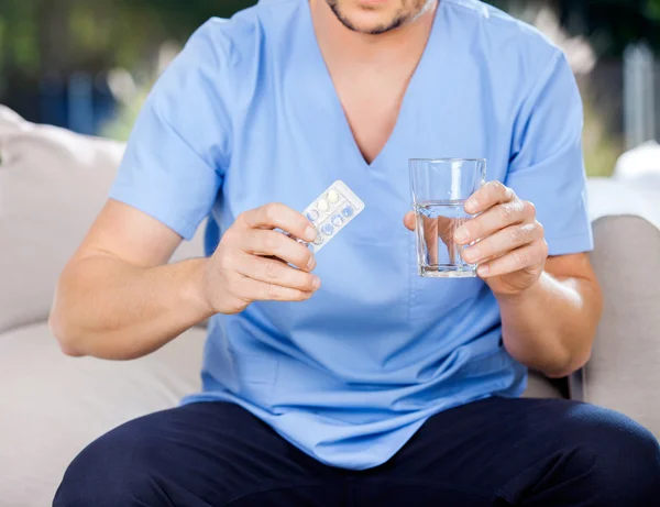 Männlicher Hausmeister mit Blisterverpackung und Glas Wasser — Stockfoto