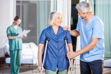 Happy Male Caretaker Helping Senior Woman In Walking clipart