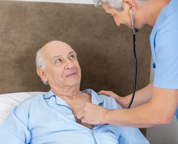 Senior Man kijken naar Caretaker onderzoeken hem met stethoscoop — Stockfoto