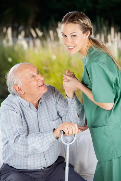 Lachende verpleegster helpen Senior Man om op te staan van Bank — Stockfoto