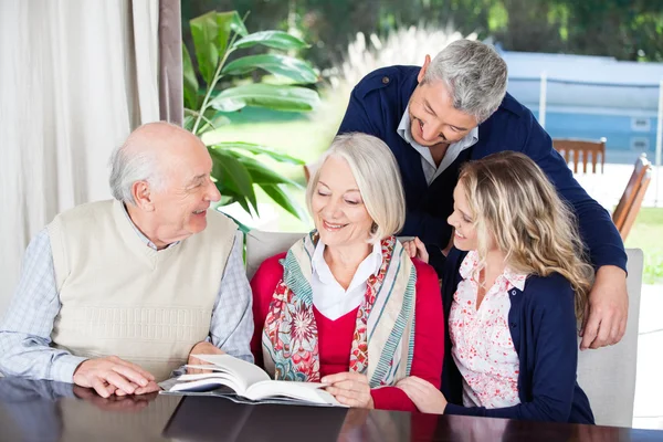 Pareja feliz con abuelos leyendo libro en el hogar de ancianos —  Fotos de Stock