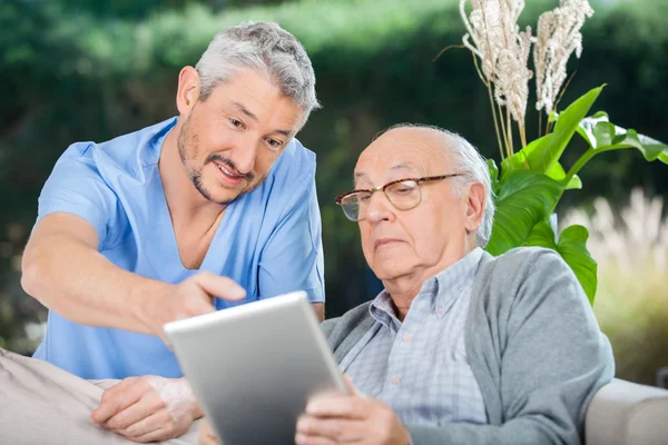 Enfermeira masculina mostrando algo ao homem sênior no tablet digital — Fotografia de Stock