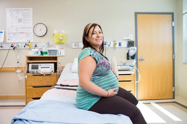 Glad gravid kvinna med händerna på magen på sjukhussäng — Stockfoto