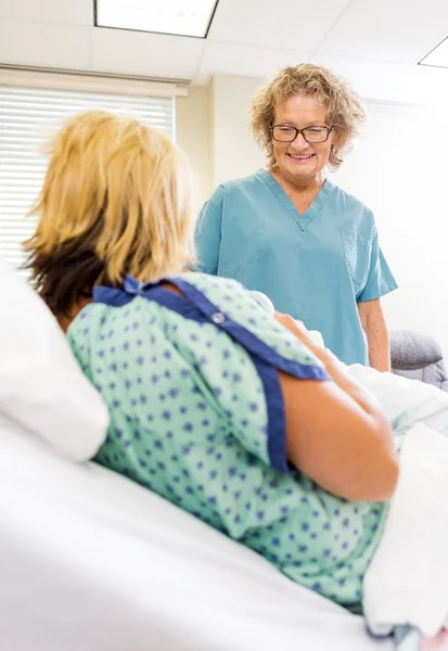 Enfermera feliz mirando bebé recién nacido con la madre en el hospital —  Fotos de Stock