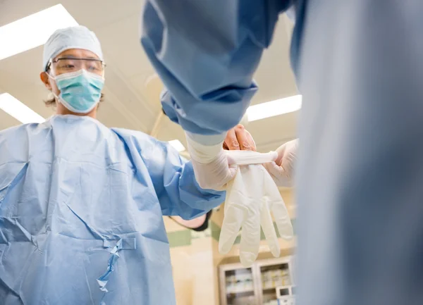 Enfermera asistiendo cirujano en el uso de guante —  Fotos de Stock