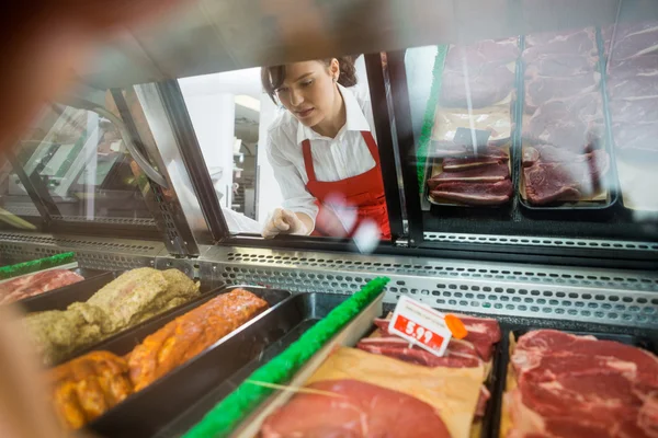 Vendedora olhando para a variedade de carne exibida na loja — Fotografia de Stock