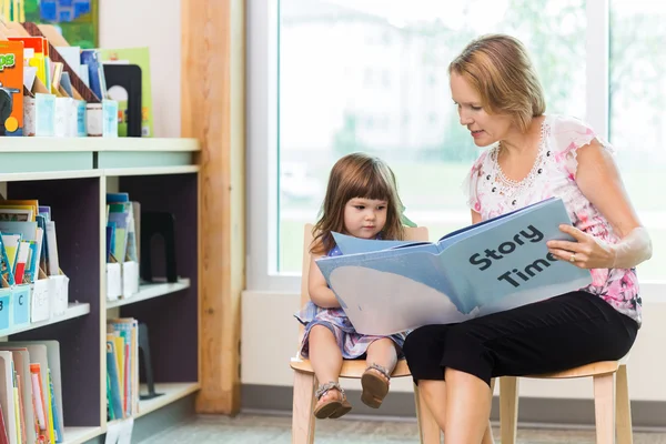 Lehrerin mit süßem Mädchen liest Buch in Bibliothek — Stockfoto