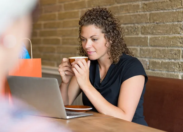 Frau schaut beim Kaffeetrinken am Cafétisch auf Laptop — Stockfoto