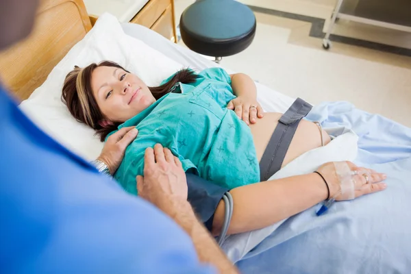 Беременная женщина улыбается, когда ее утешает муж в больнице — стоковое фото