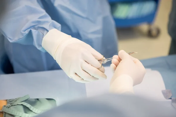 Cirurgiões passando tesouras cirúrgicas durante a cirurgia — Fotografia de Stock