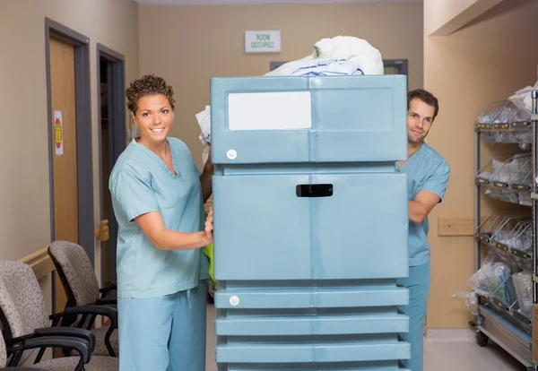 Krankenschwestern schieben mit Bettwäsche gefüllten Einkaufswagen in Krankenhausflur — Stockfoto