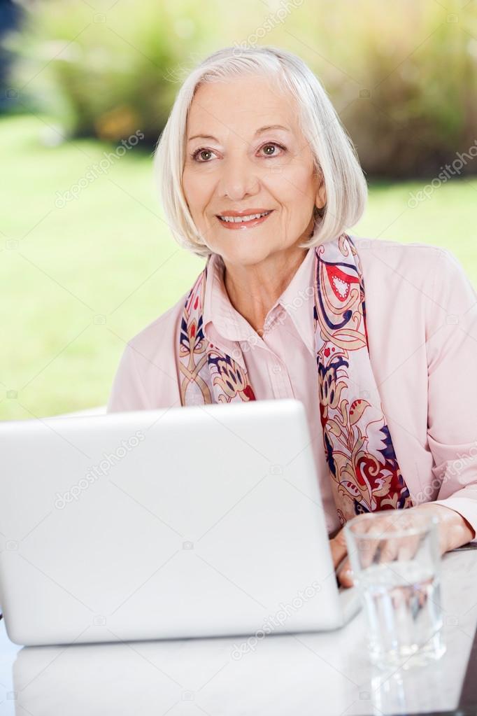 Smiling Elderly Woman Looking Away While Using Laptop On Porch