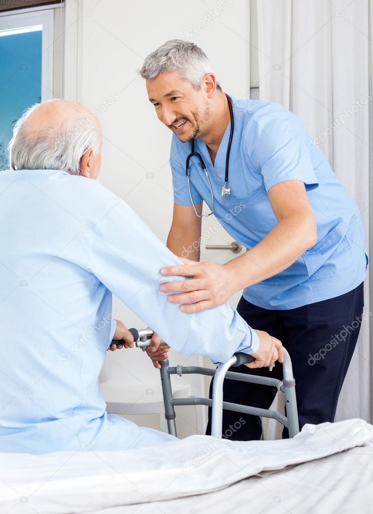 Caretaker Assisting Senior Man To Use Walking Frame