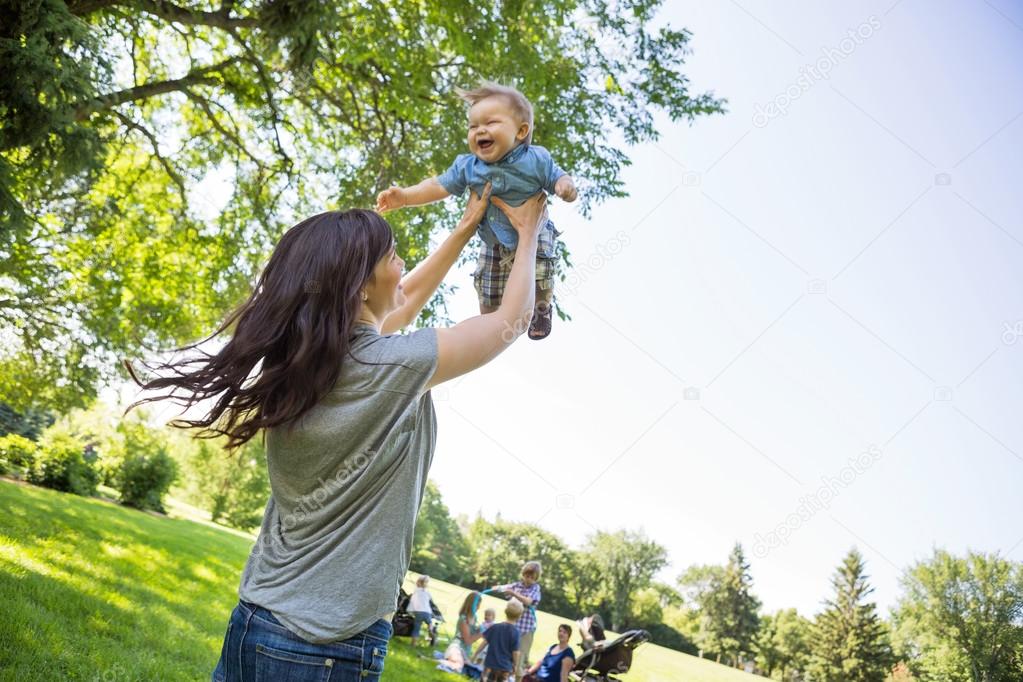 Playful Young Mother Lifting Baby Boy At Park