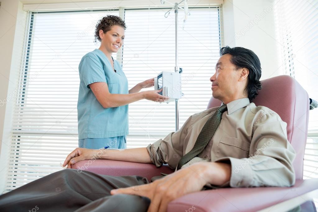 Nurse Looking At Patient While Adjusting IV Machine
