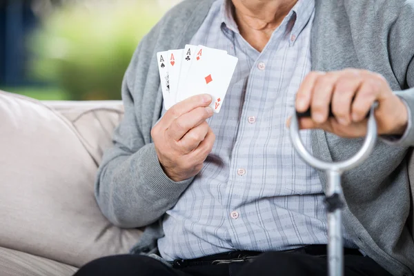 Homme âgé montrant quatre as tout en étant assis — Photo