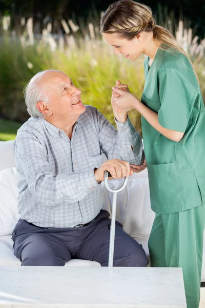 Cuidador femenino que ayuda al anciano a levantarse del sofá —  Fotos de Stock