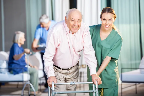 Femmina custode aiutare anziano uomo in utilizzando Zimmer telaio — Foto Stock