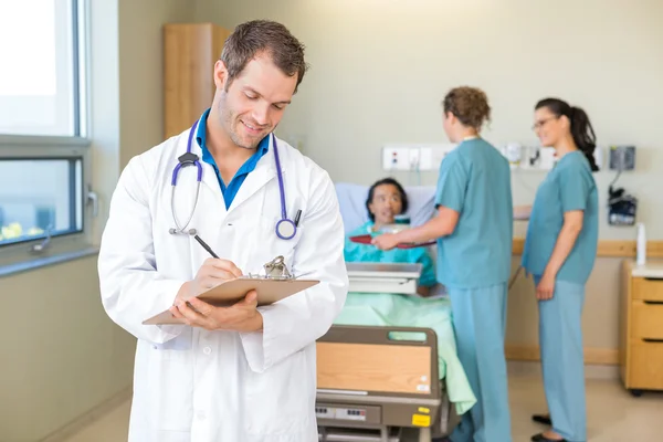 Docteur écrit sur presse-papiers avec les infirmières et le patient à l'hôpital — Photo