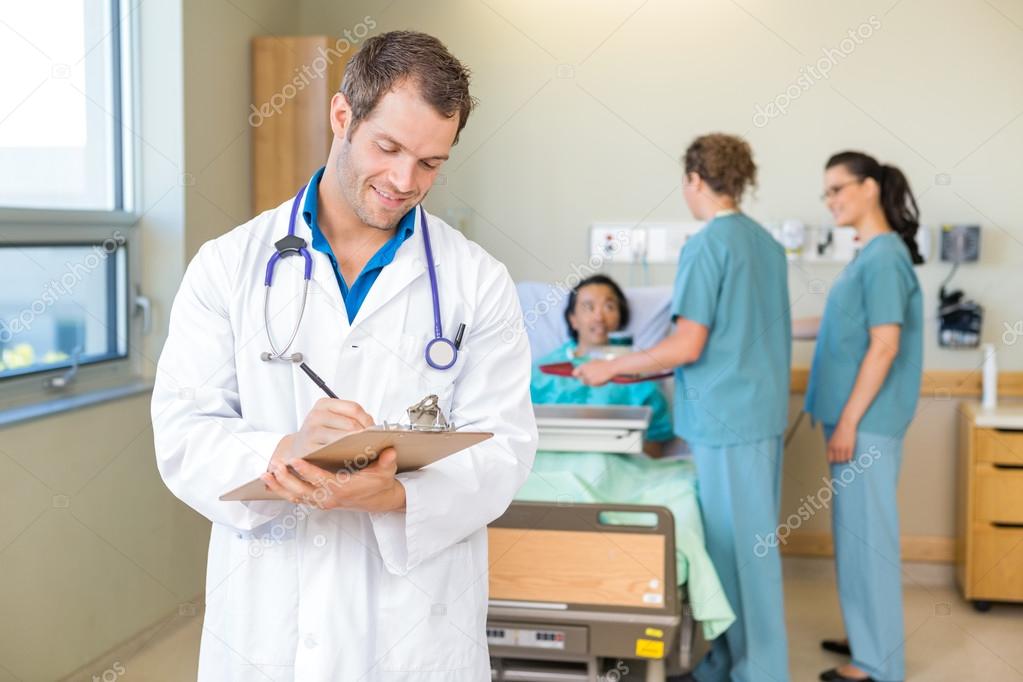 Doctor Writing On Clipboard With Nurses And Patient In Hospital