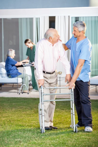 Смотритель утешает пожилого человека, помогая ему на лужайке — стоковое фото