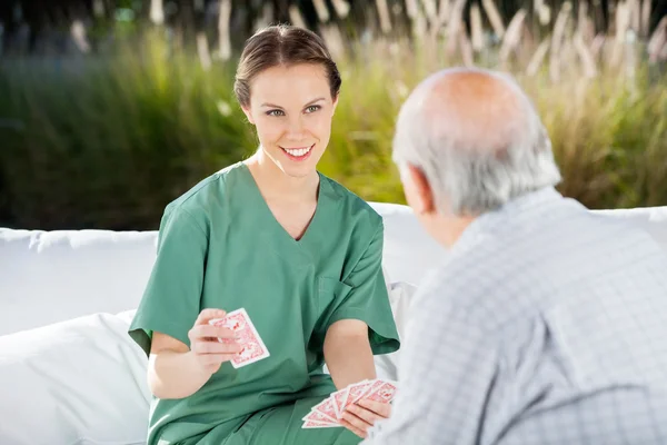 Enfermera sonriente jugando a las cartas con un hombre mayor —  Fotos de Stock