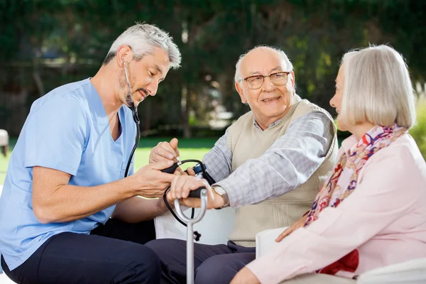 Médecin mesurant la pression artérielle de l'homme âgé assis à côté de Wom — Photo