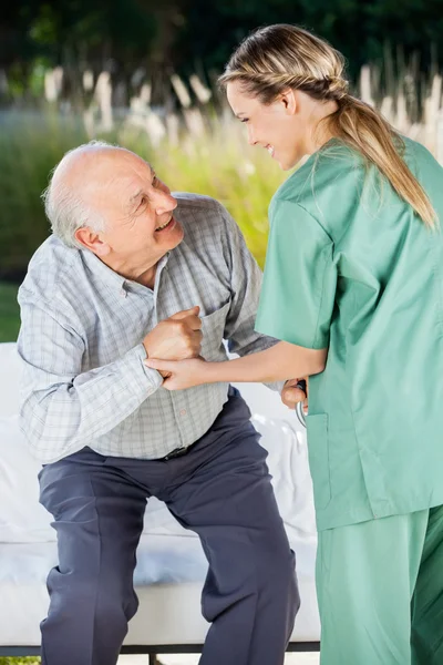 Krankenschwester hilft Seniorin auf Couch zu sitzen — Stockfoto