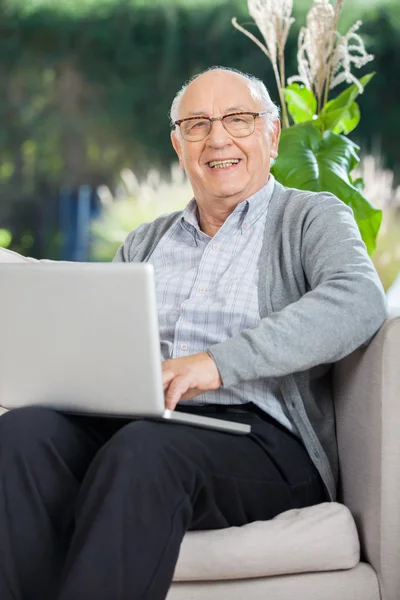 Feliz homem sênior sentado com laptop no sofá — Fotografia de Stock