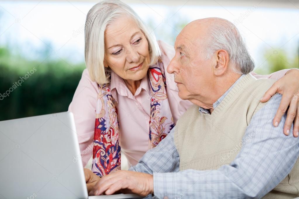 Senior Couple Looking At Each Other While Using Laptop