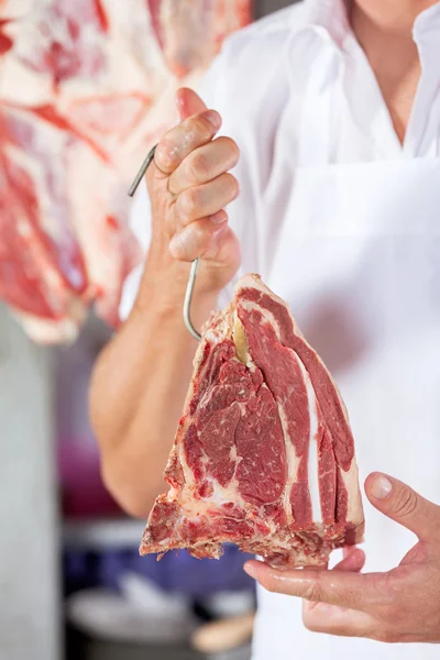 Мясник держит сырое мясо с крюком — стоковое фото