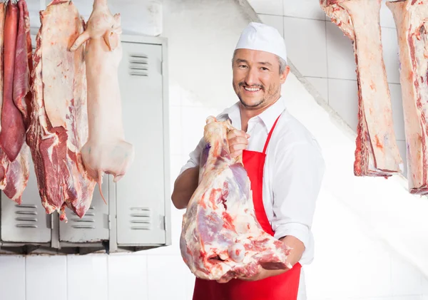 Carniceiro feliz transportando carne no açougue — Fotografia de Stock