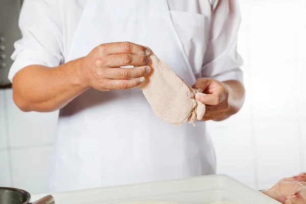 Carnicero sosteniendo carne de pollo cubierta con harina — Foto de Stock