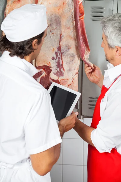 Мясники анализируют мясо, висящее в мясной лавке — стоковое фото